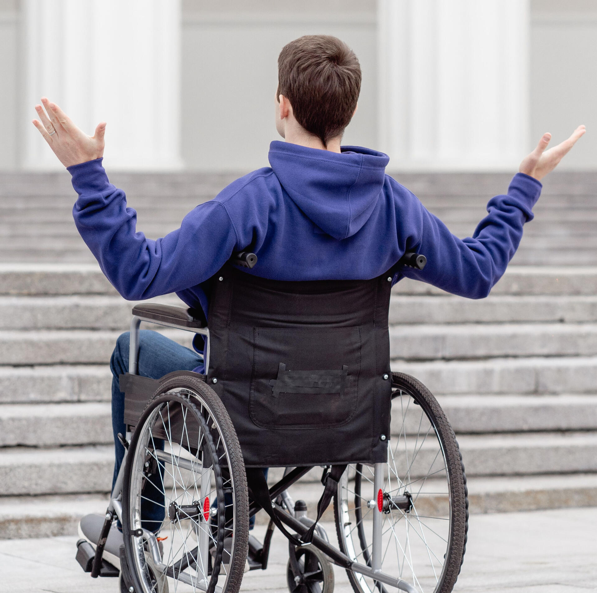 Man in a wheelchair throwing his arms up at a set of stairs