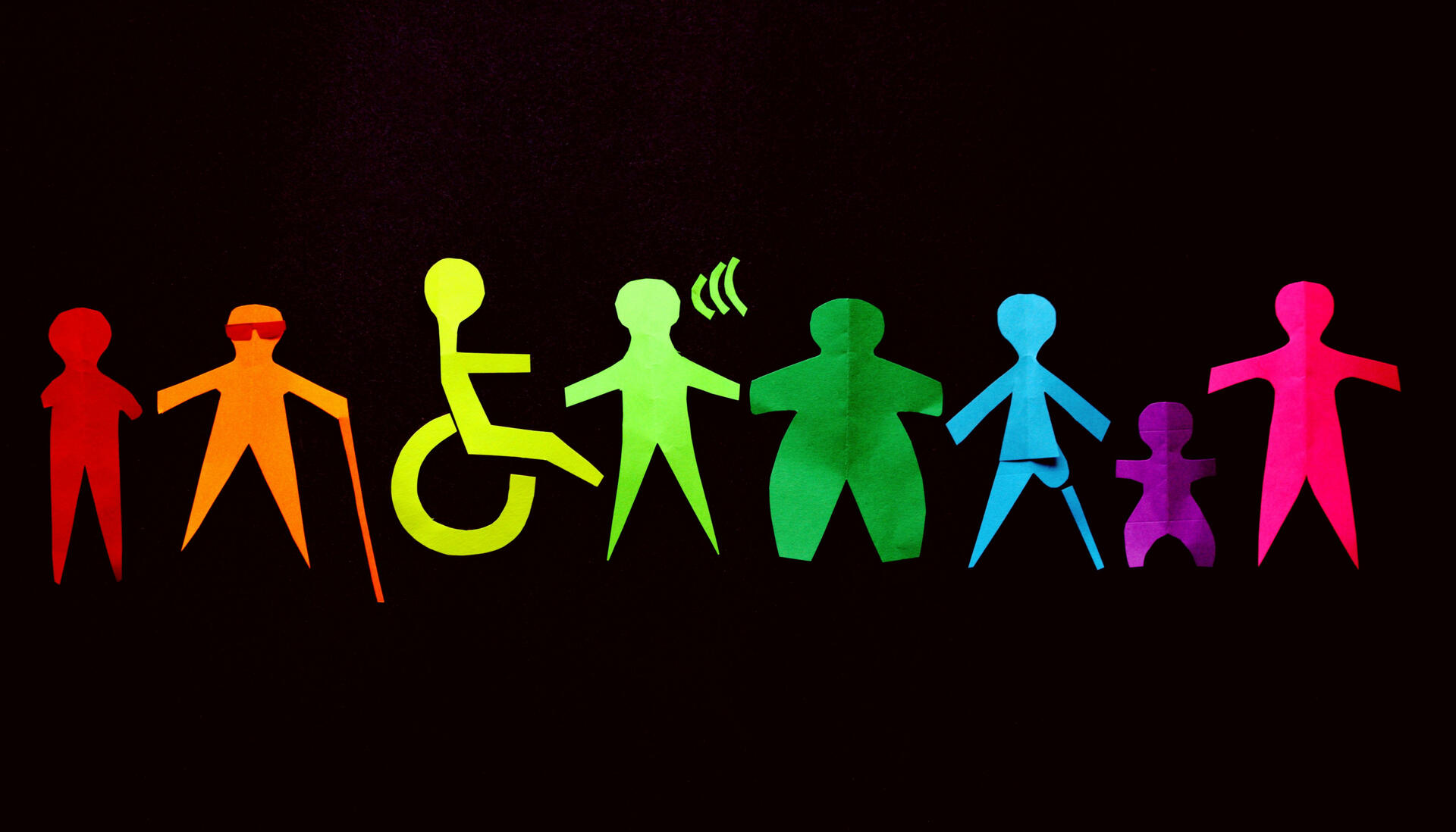 Paper cutouts of people with various disabilities, in the colors of the rainbow.